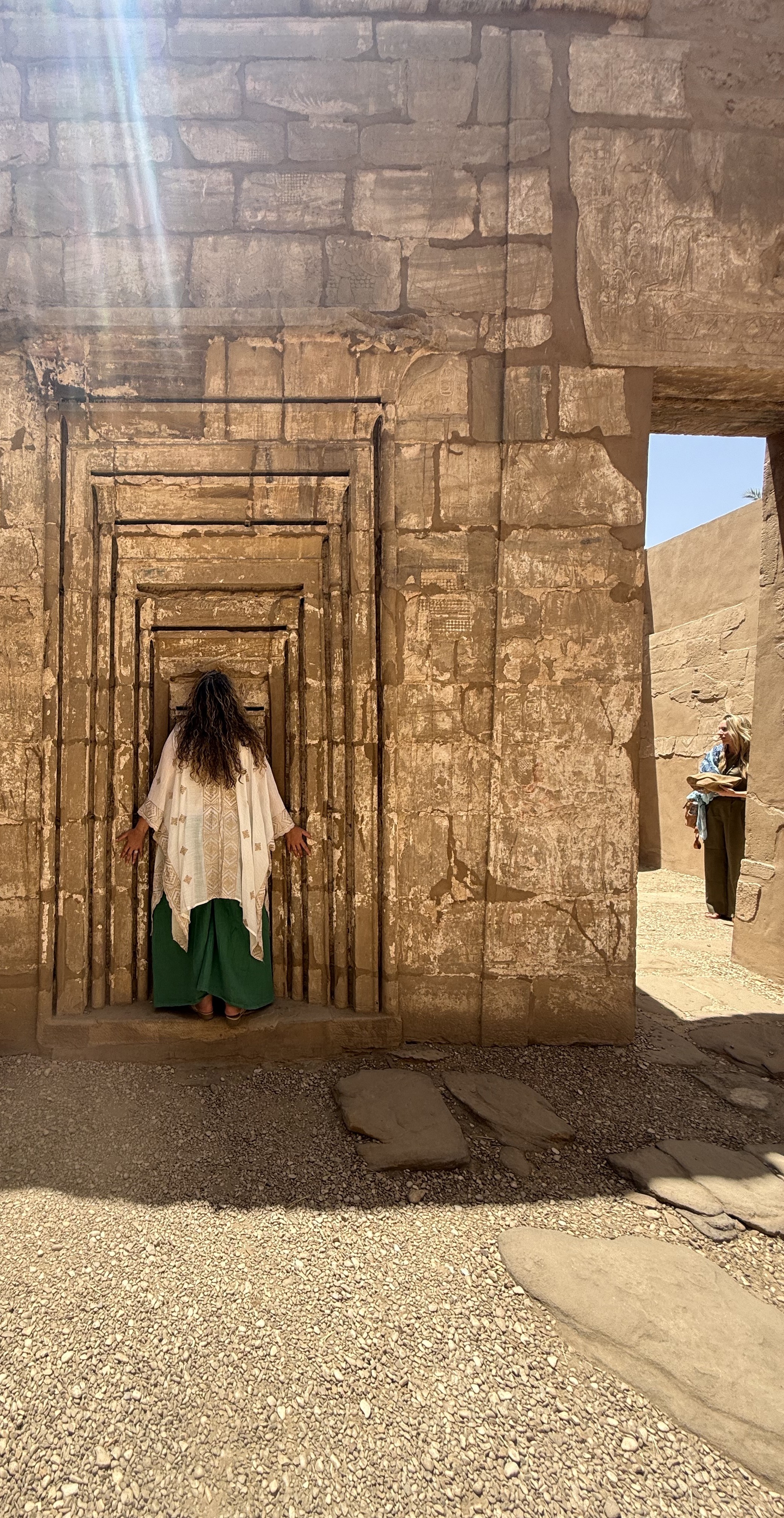 A woman standing in prayerful stillness at an ancient Egyptian temple doorway